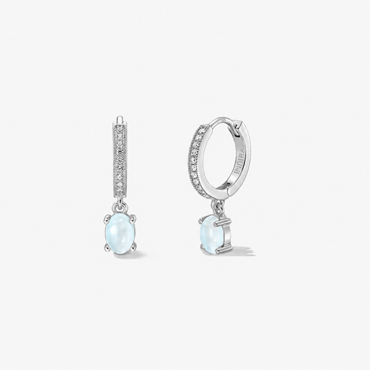 Boucles d'oreilles huggie en argent 925 avec cercles pavés et pendants en pierre de lune ovale bleu laiteux ; paire photographiée sur fond blanc, vues de face et de profil.
