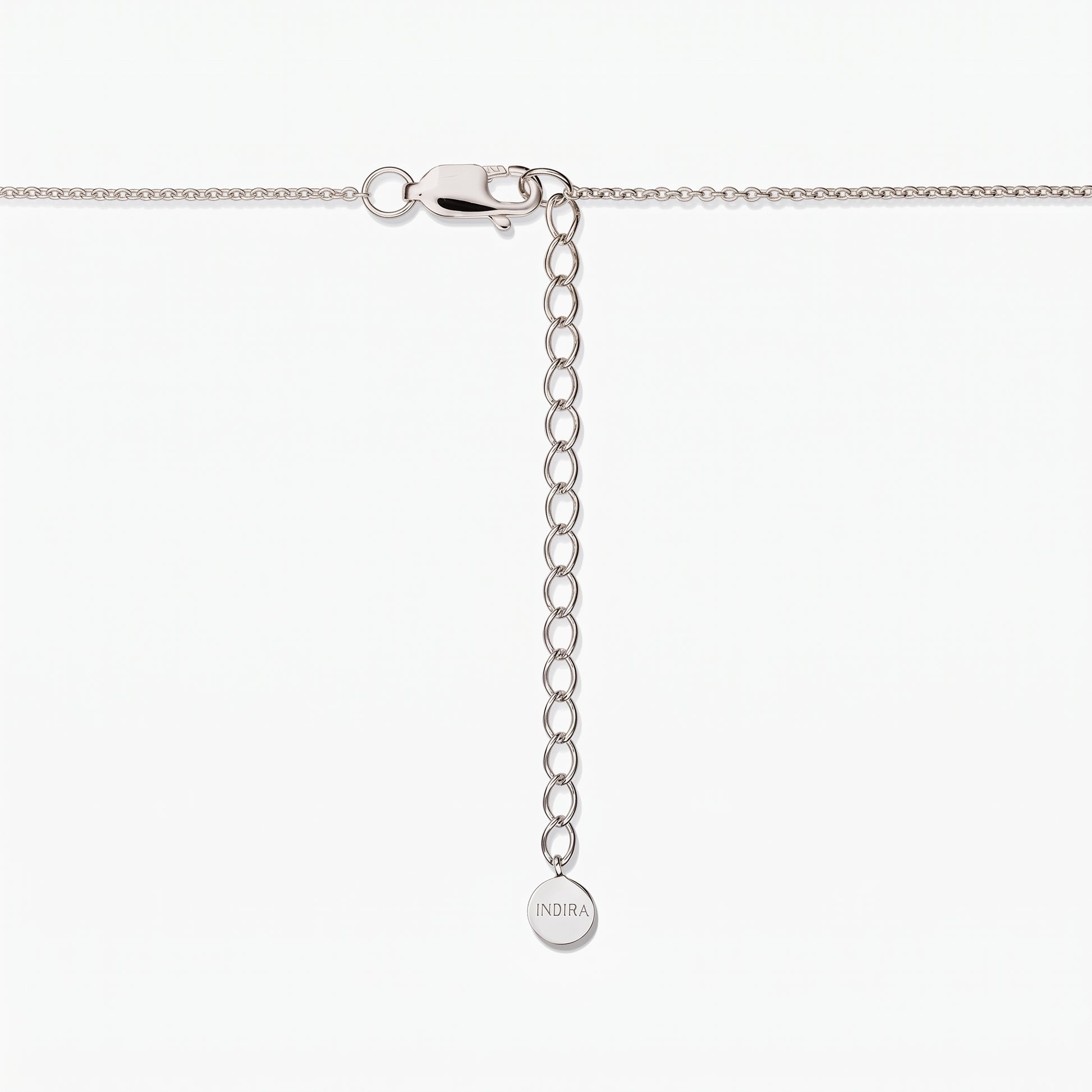 Gros plan sur un fermoir de collier en argent sterling avec une chaîne d’extension réglable et une petite plaque ronde gravée « INDIRA », sur fond blanc.