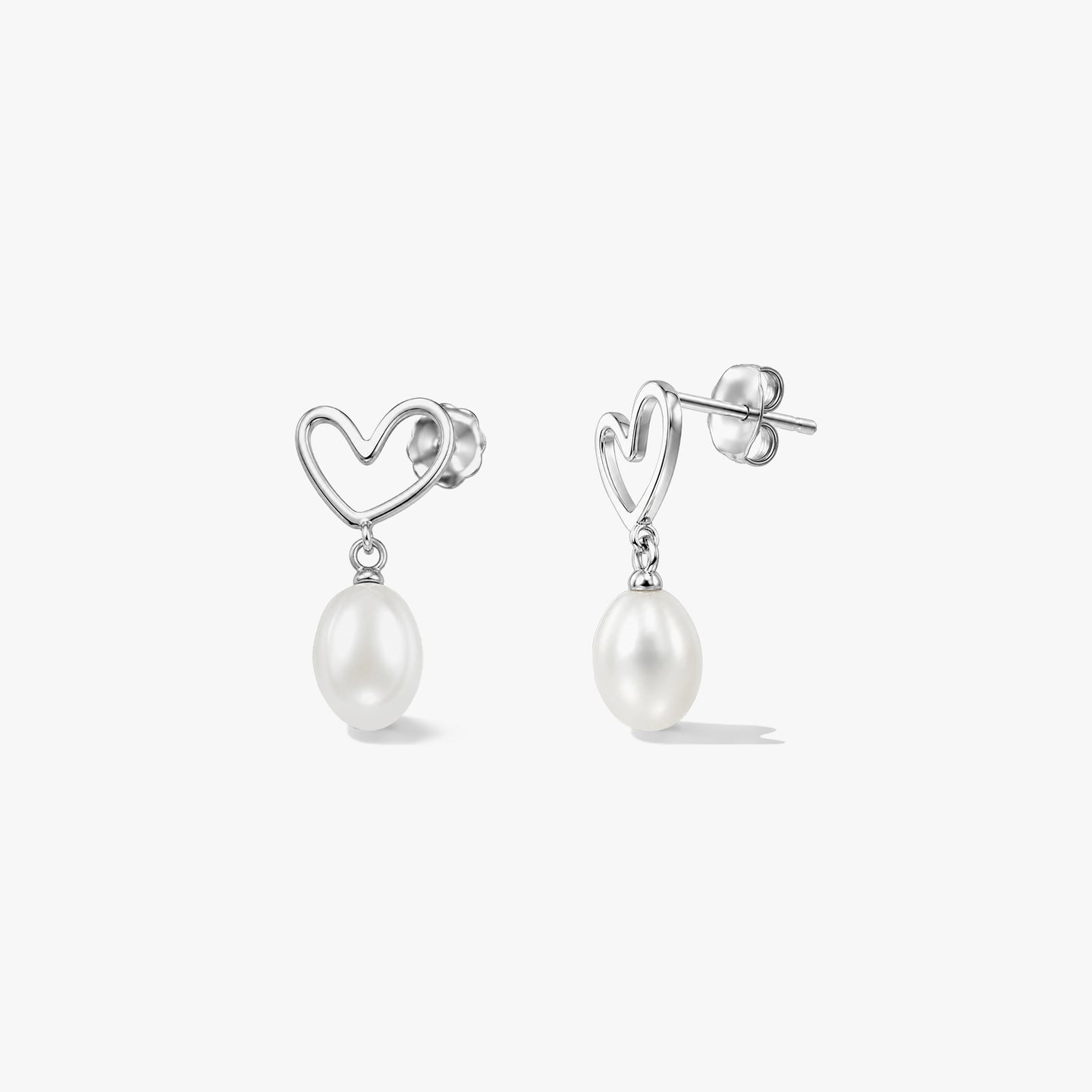 Paire de clous d’oreilles en argent sterling en forme de cœur, ornés de perles blanches naturelles pendantes, sur fond blanc.