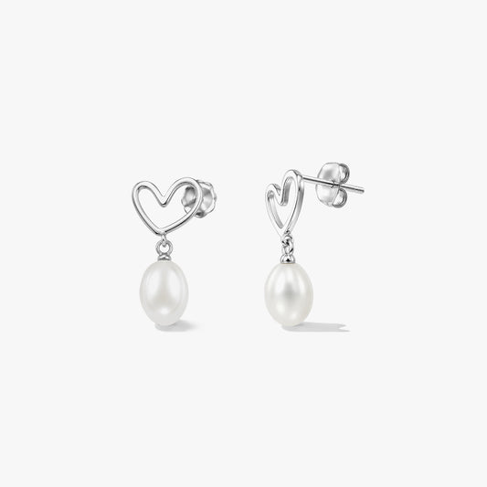 Paire de clous d’oreilles en argent sterling en forme de cœur, ornés de perles blanches naturelles pendantes, sur fond blanc.