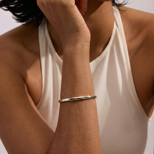 Un gros plan d'une personne portant un bracelet Serena en argent sur le bras, sur un fond uni.