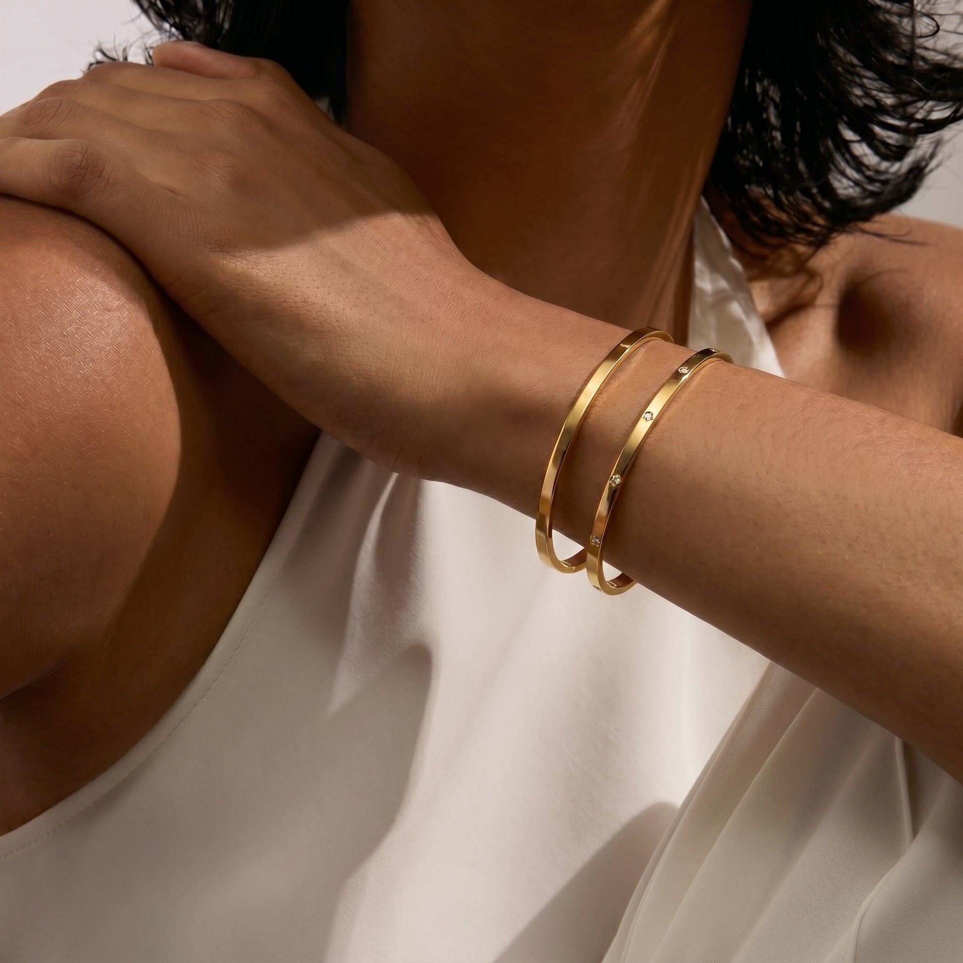 Gros plan sur le bras d'une personne portant deux bracelets en or sur fond blanc.