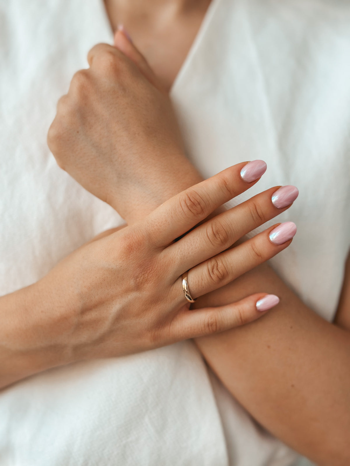 Gros plan d'une main portant une large alliance en or arrondie avec un nail art rose et argenté.