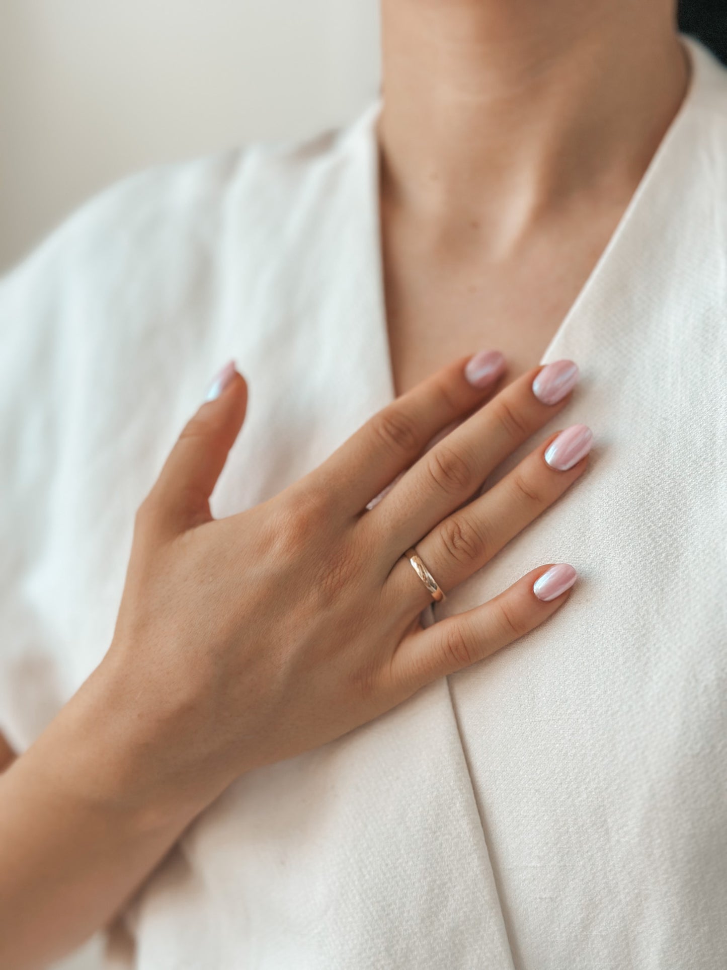 Gros plan sur une main avec une alliance en or et des ongles manucurés sur un tissu blanc.