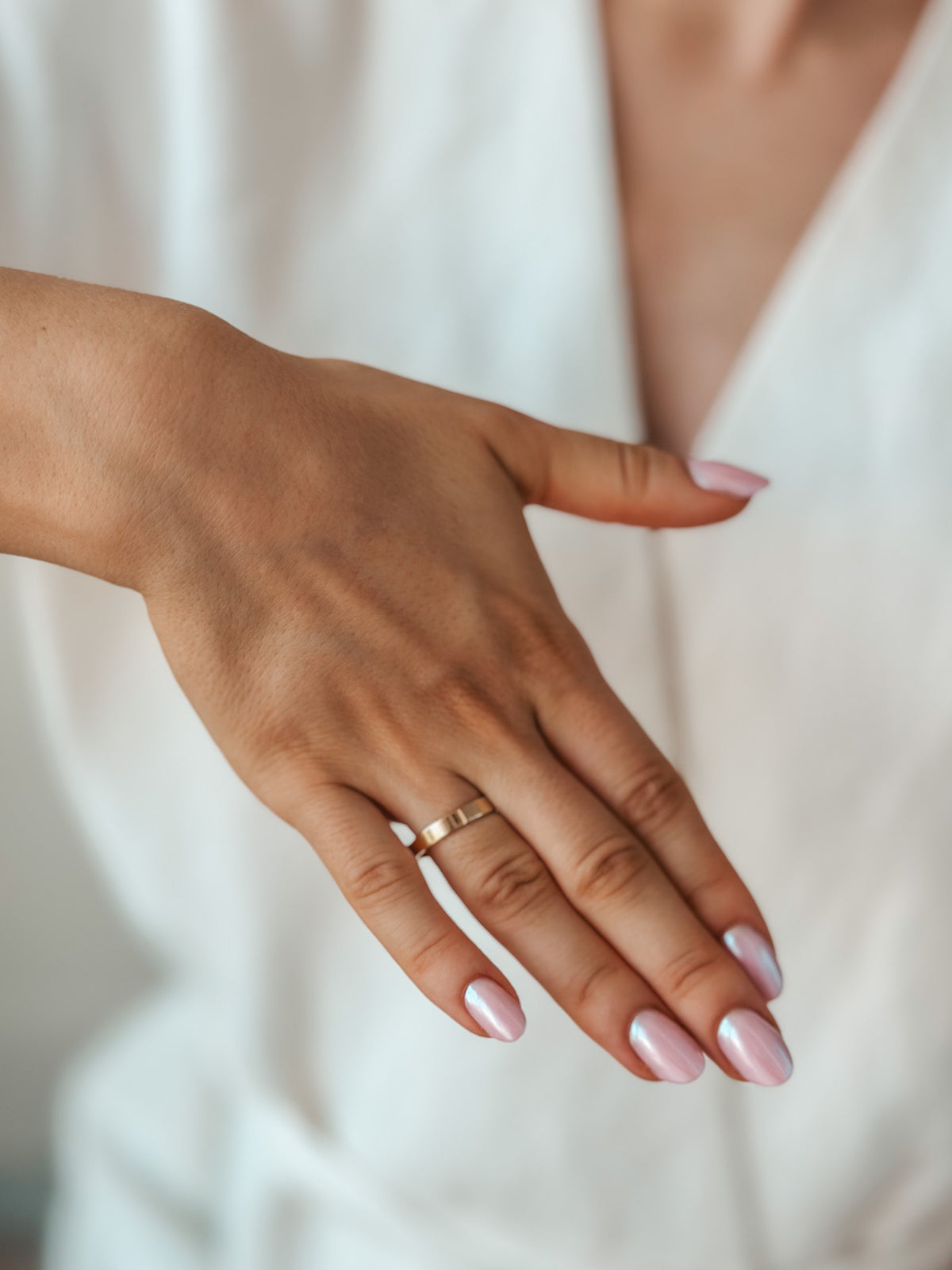 Une main présentant une simple alliance en or avec des ongles manucurés rose.