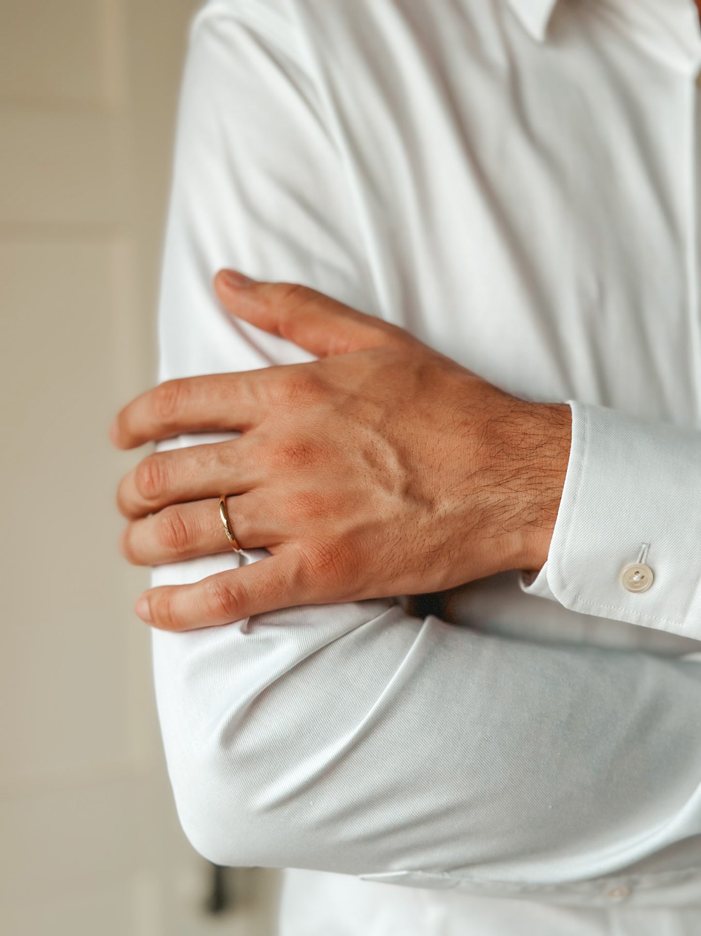 Gros plan sur une personne portant une chemise blanche et une fine alliance en or à son doigt.