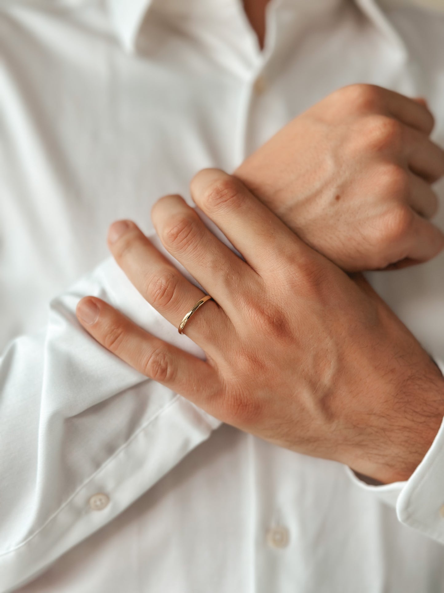 Gros plan sur une personne portant une fine alliance en or arrondie sur sa main par-dessus une chemise blanche.