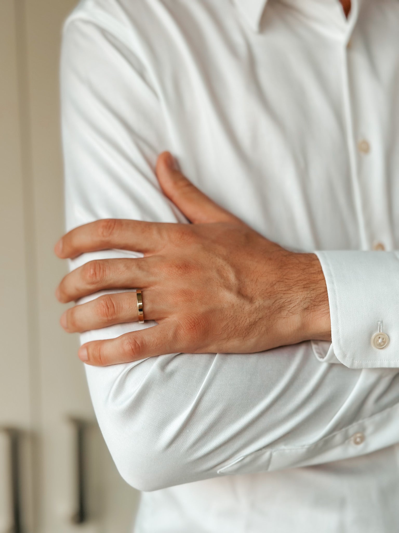 Gros plan sur le bras d'un homme portant une simple alliance en or sur une chemise blanche.