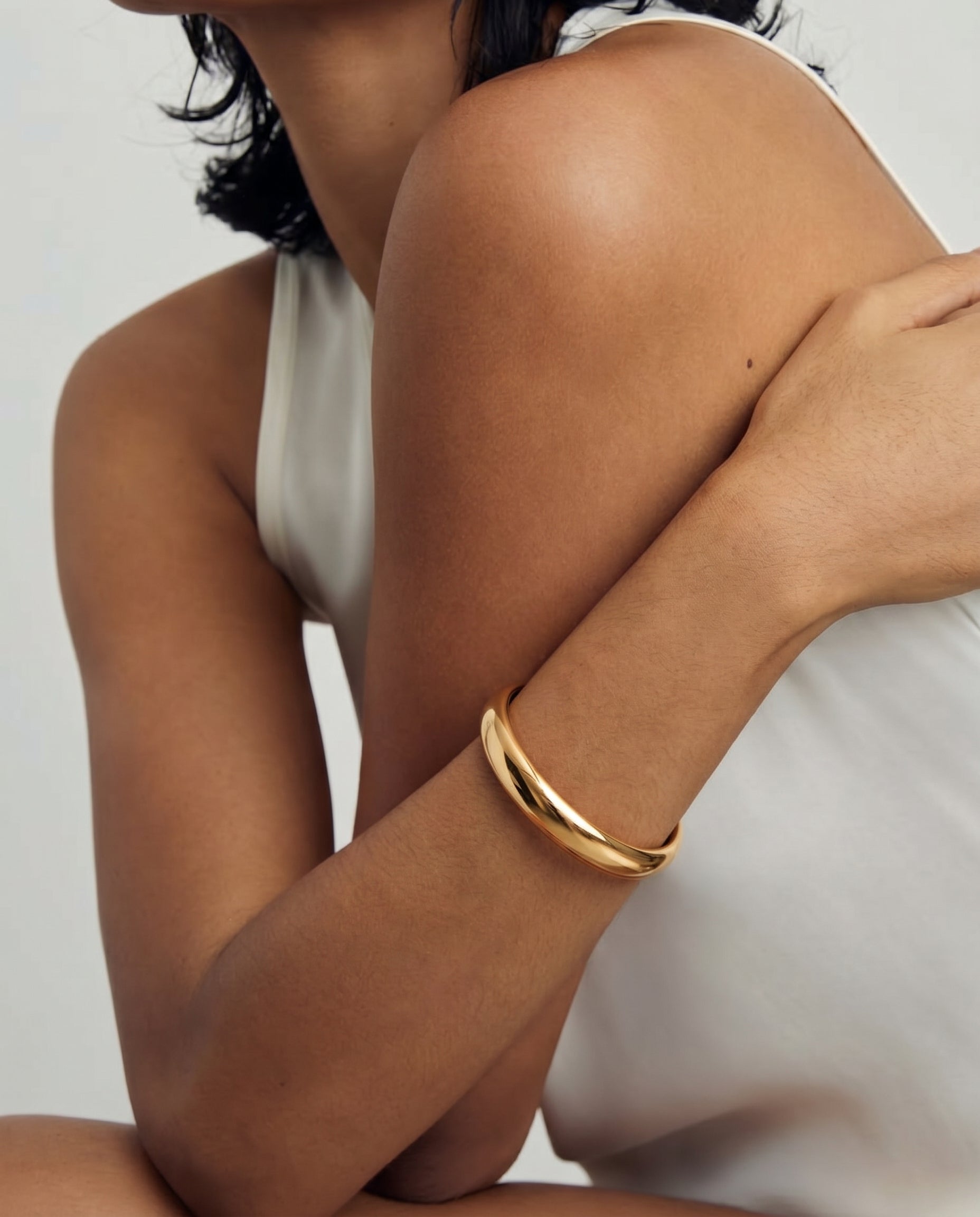 Gros plan d'une personne portant un bracelet jonc plaqué or sur le bras, sur un fond blanc.