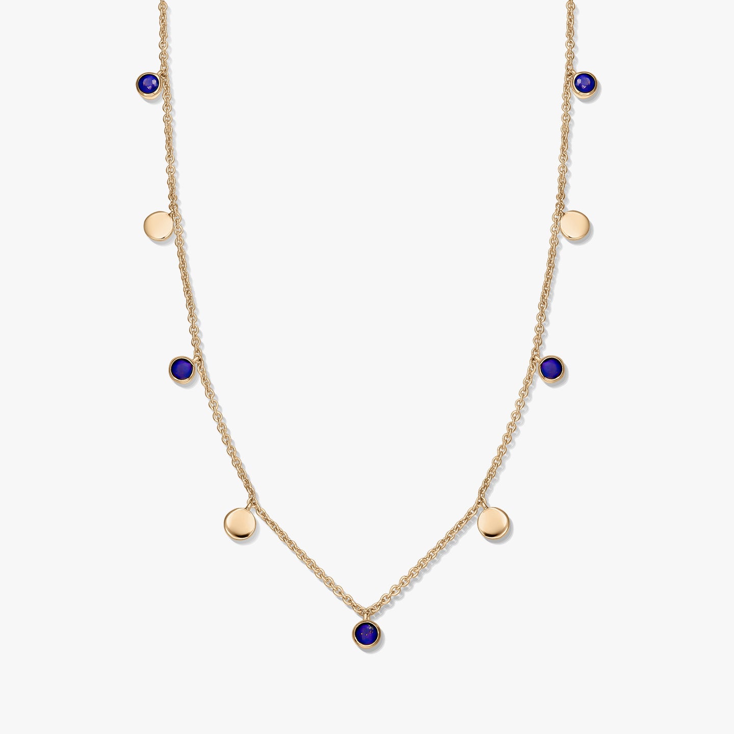 Collier à stations en argent sterling plaqué or avec cabochons ronds en lapis-lazuli et de petites breloques en forme de disque en or sur une chaîne délicate, photographié sur fond blanc.
