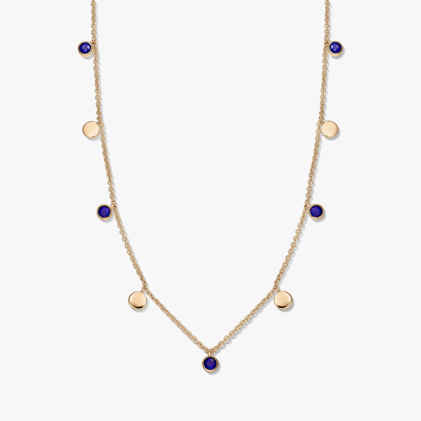 Collier à stations en argent sterling plaqué or avec cabochons ronds en lapis-lazuli et de petites breloques en forme de disque en or sur une chaîne délicate, photographié sur fond blanc.