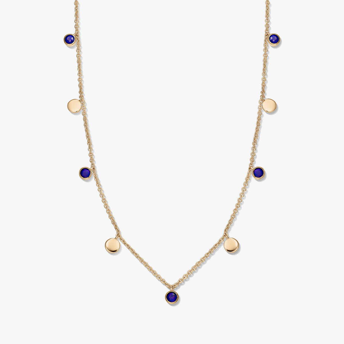 Collier à stations en argent sterling plaqué or avec cabochons ronds en lapis-lazuli et de petites breloques en forme de disque en or sur une chaîne délicate, photographié sur fond blanc.