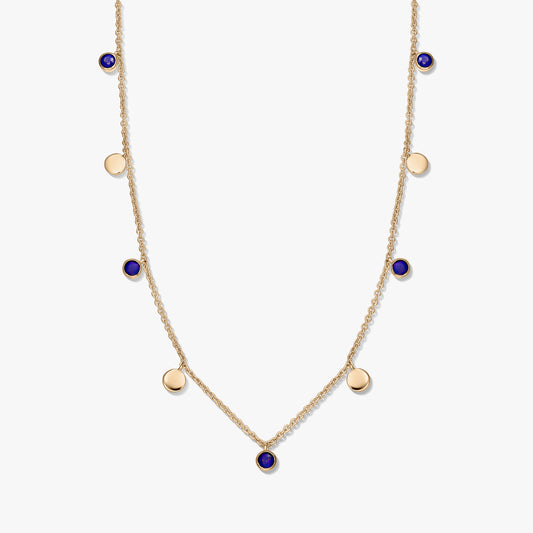 Collier à stations en argent sterling plaqué or avec cabochons ronds en lapis-lazuli et de petites breloques en forme de disque en or sur une chaîne délicate, photographié sur fond blanc.