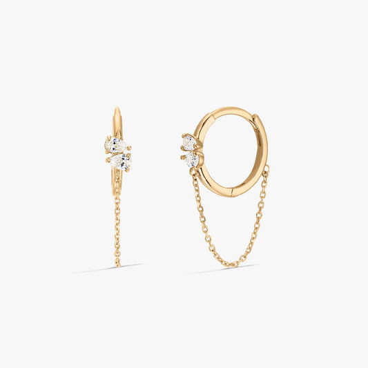 Boucles d'oreilles créoles en or élégantes avec des zircons et un détail chaîne sur fond blanc.