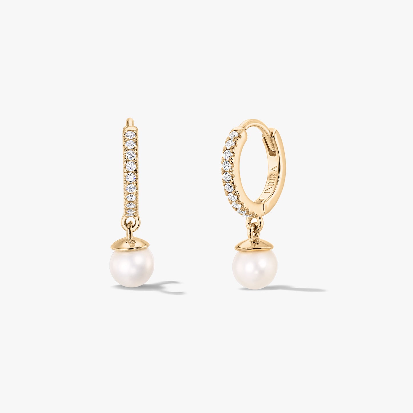 Paire de créoles huggie en argent doré serties d’un pavé d’oxydes de zirconium, avec pendentifs en perles naturelles blanches, par Indira, présentées de face et de profil sur fond blanc.