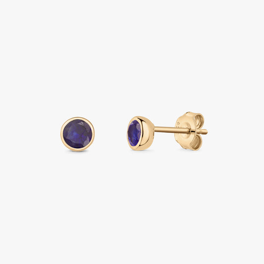Paire de puces d’oreilles en saphir, pierre de naissance de septembre, en argent avec un serti clos doré, présentées sur fond blanc.