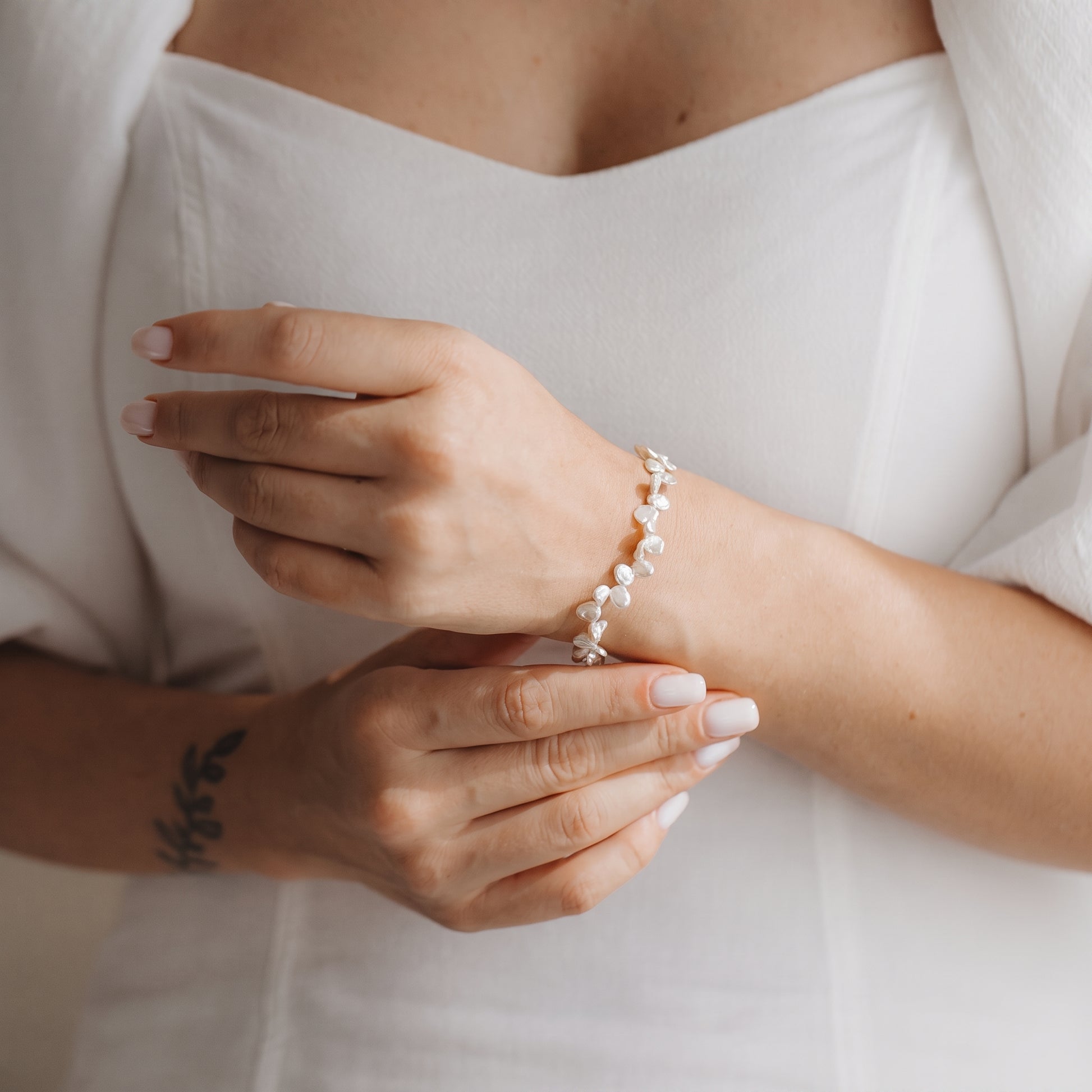 Gros plan sur des mains portant un bracelet en argent sterling plaqué or, orné de perles keshi blanches, sur fond d’une robe blanche.