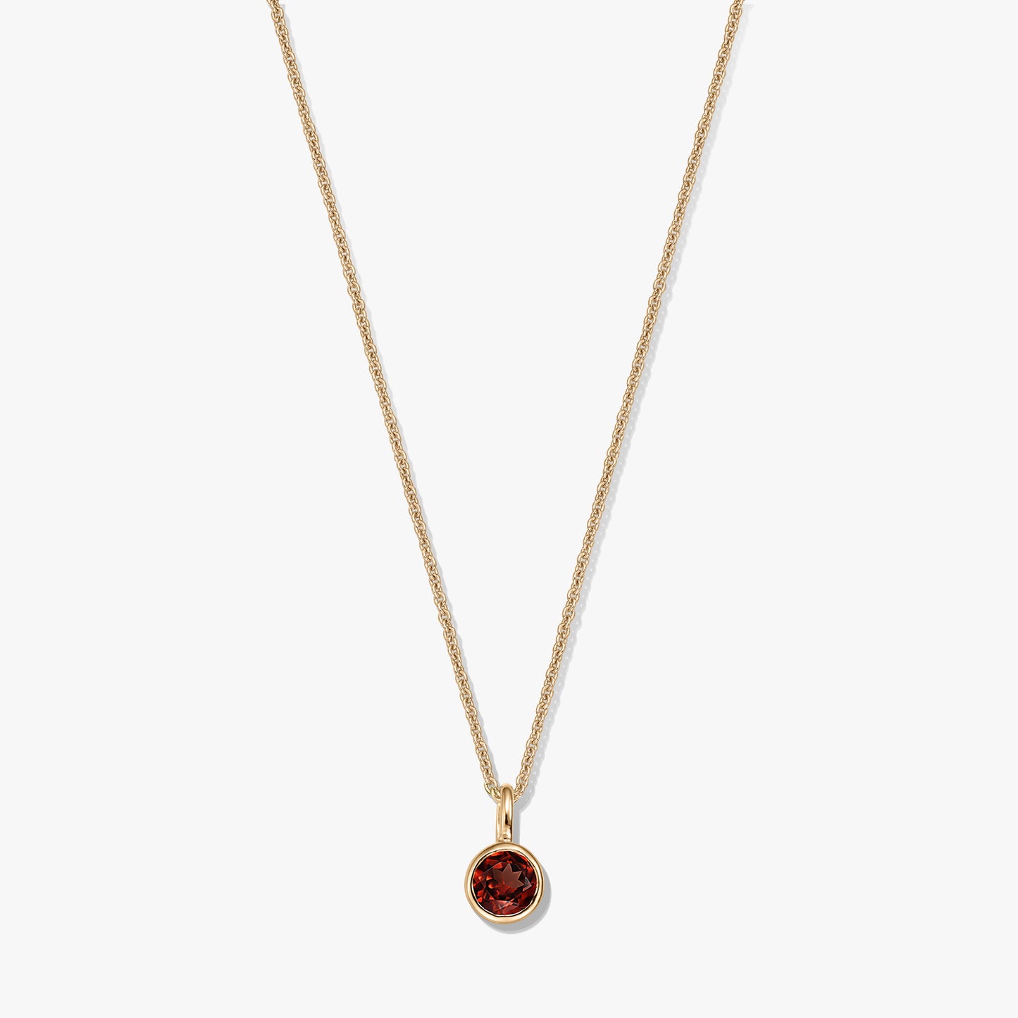Collier élégant en argent sterling plaqué or avec pendentif en grenat rond serti clos sur une chaîne délicate, isolé sur fond blanc.