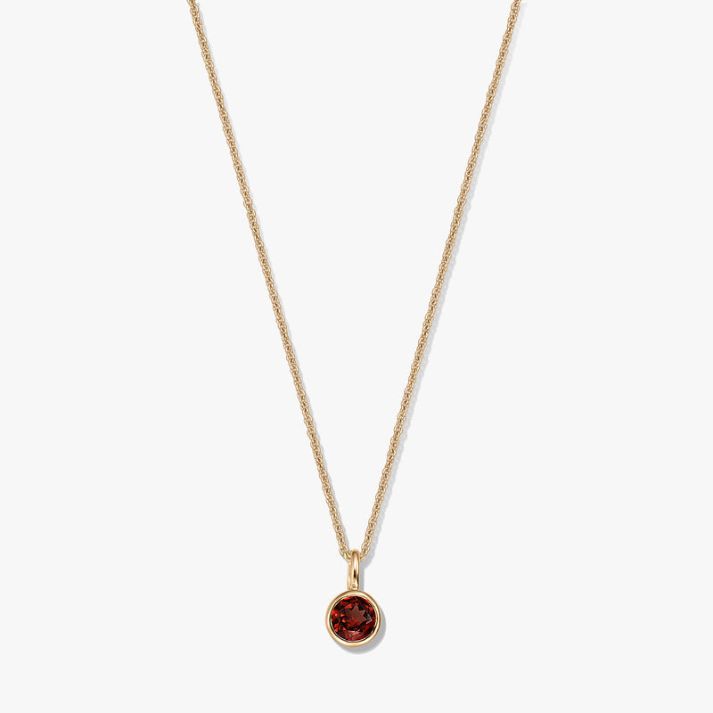 Collier élégant en argent sterling plaqué or avec pendentif en grenat rond serti clos sur une chaîne délicate, isolé sur fond blanc.