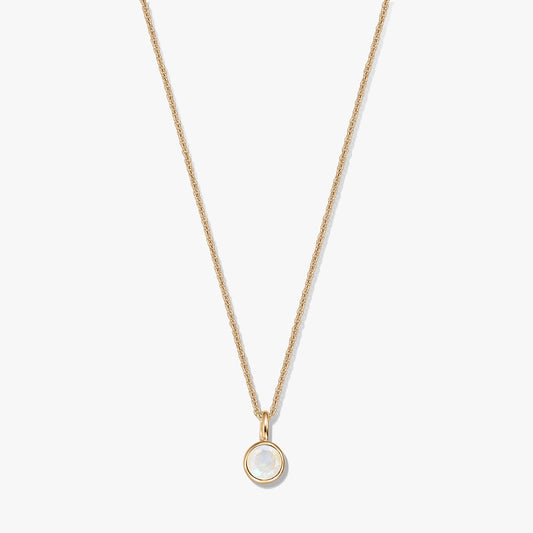 Collier en argent sterling plaqué or avec un petit pendentif pierre de naissance en pierre de lune ronde sertie dans un chaton, centré sur un fond blanc.