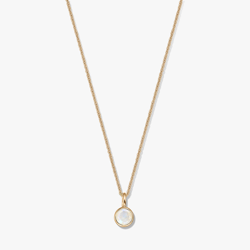 Collier en argent sterling plaqué or avec un petit pendentif pierre de naissance en pierre de lune ronde sertie dans un chaton, centré sur un fond blanc.