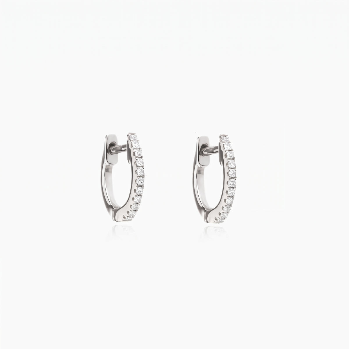 Paire de boucles d’oreilles créoles huggie Sadie en argent avec zirconia clair pavé sur fond blanc.