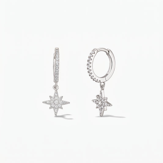 Paire de créoles huggie en argent sterling 925 avec pendentifs Étoile du Nord pavés d'oxydes de zirconium blancs, sur fond blanc.