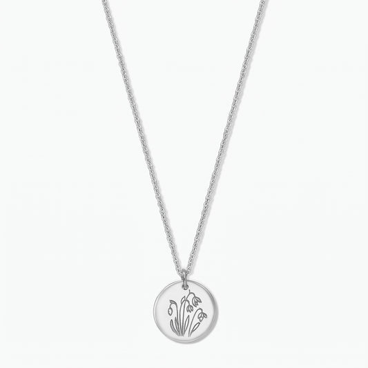 Collier fleur de naissance en argent sterling avec un pendentif disque rond gravé de perce-neige de janvier sur une chaîne fine, isolé sur fond blanc.