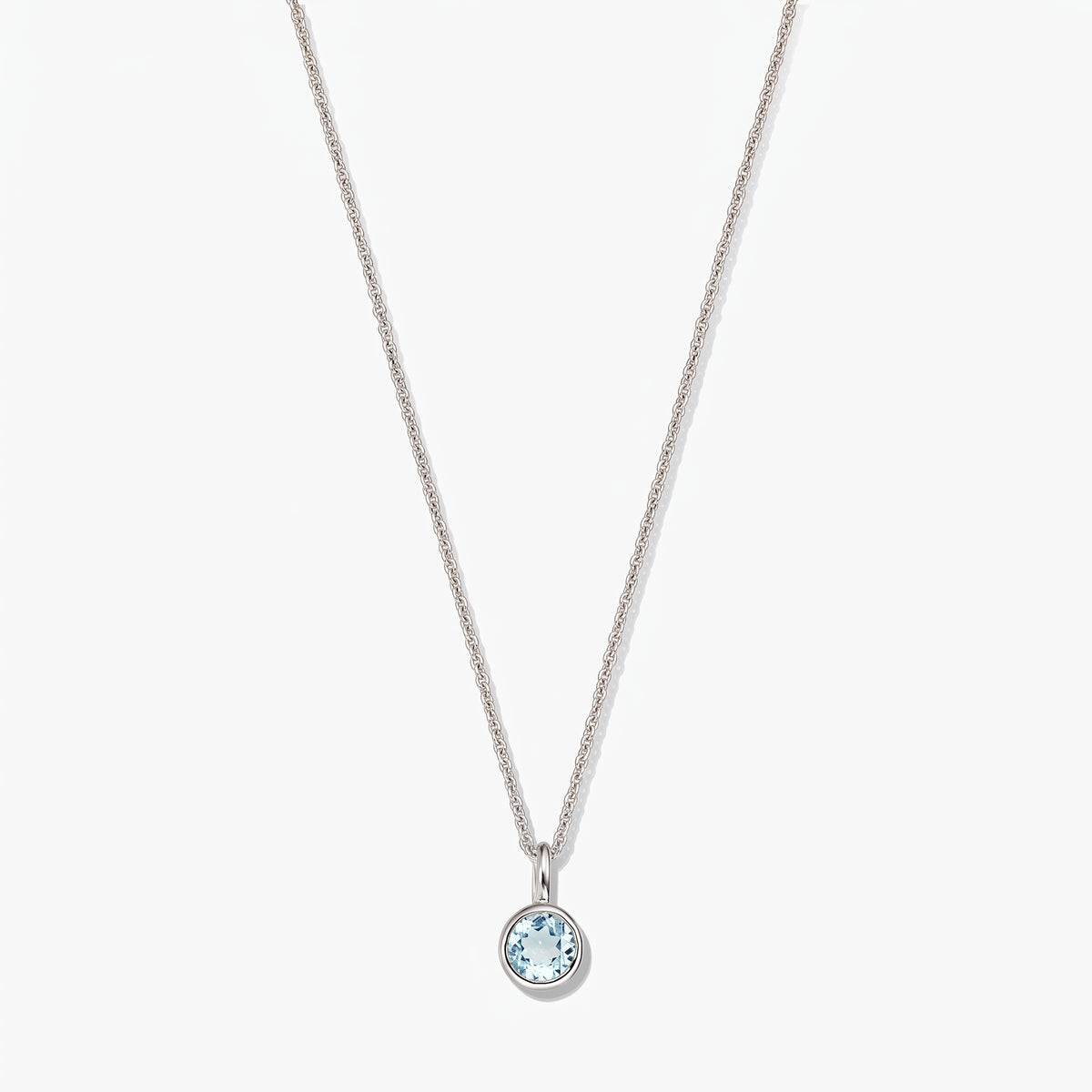 Collier en argent sterling avec pierre de naissance, petit pendentif rond en topaze bleue monté en serti clos, sur fond blanc.