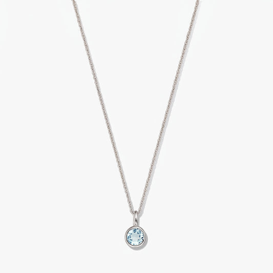 Collier en argent sterling avec pierre de naissance, petit pendentif rond en topaze bleue monté en serti clos, sur fond blanc.