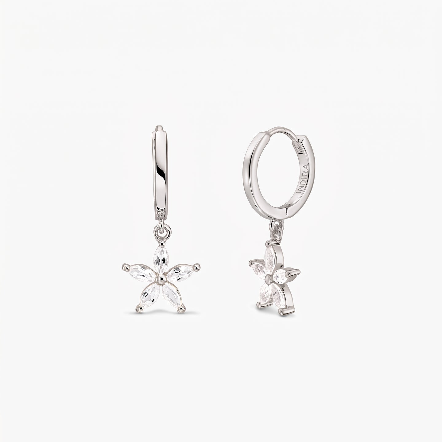Paire de créoles huggie en argent sterling, ornées de breloques fleur à cinq pétales serties de topaze blanche, sur fond blanc.