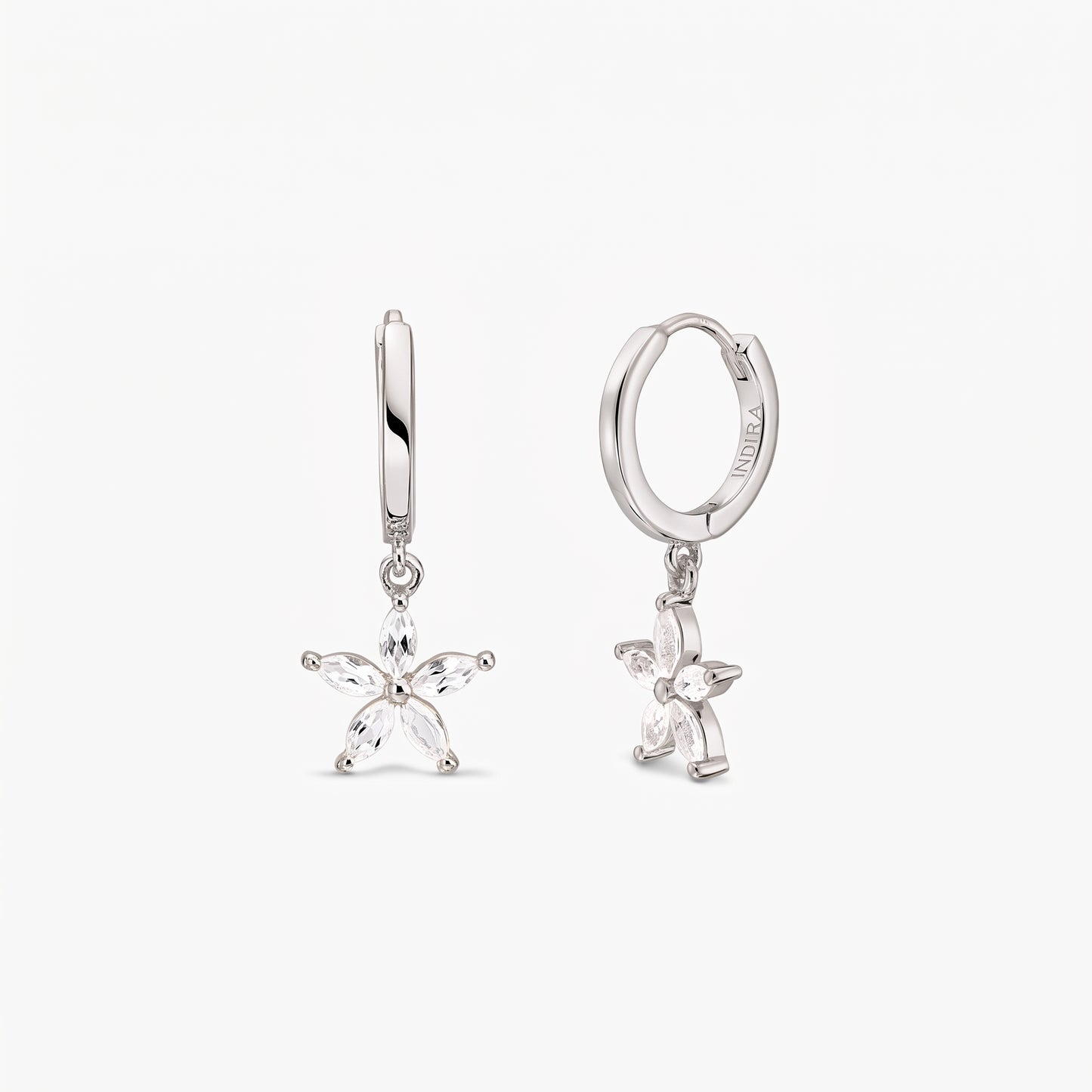 Paire de créoles huggie en argent sterling, ornées de breloques fleur à cinq pétales serties de topaze blanche, sur fond blanc.