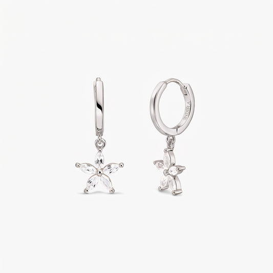 Paire de créoles huggie en argent sterling, ornées de breloques fleur à cinq pétales serties de topaze blanche, sur fond blanc.
