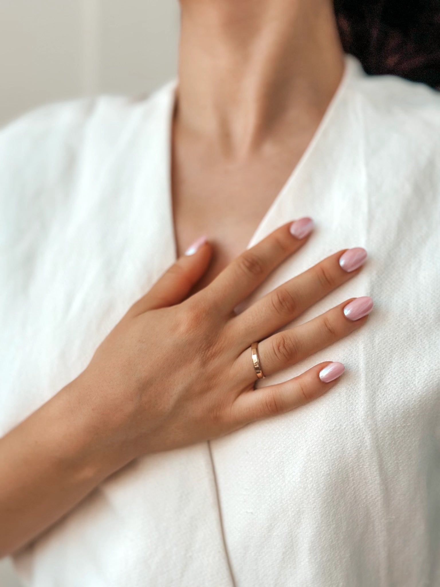 Gros plan d'une main aux ongles manucurés reposant sur une poitrine, portant une large alliance en or.