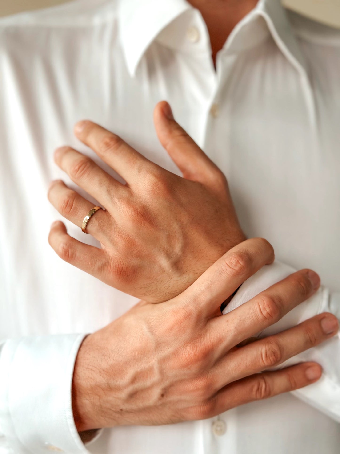 Gros plan sur des mains portant une alliance en or sur fond de chemise blanche.