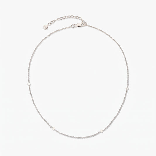 Collier chaîne en argent délicat avec de petites perles blanches espacées, présenté en cercle sur fond blanc avec une rallonge ajustable et un fermoir mousqueton.